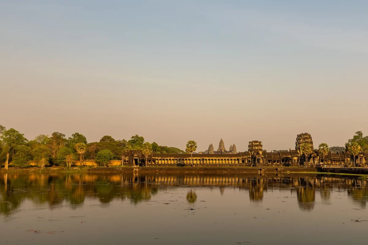 Majestic Angkor Wat temple reflecting in calm waters at sunrise, showcasing ancient architecture.