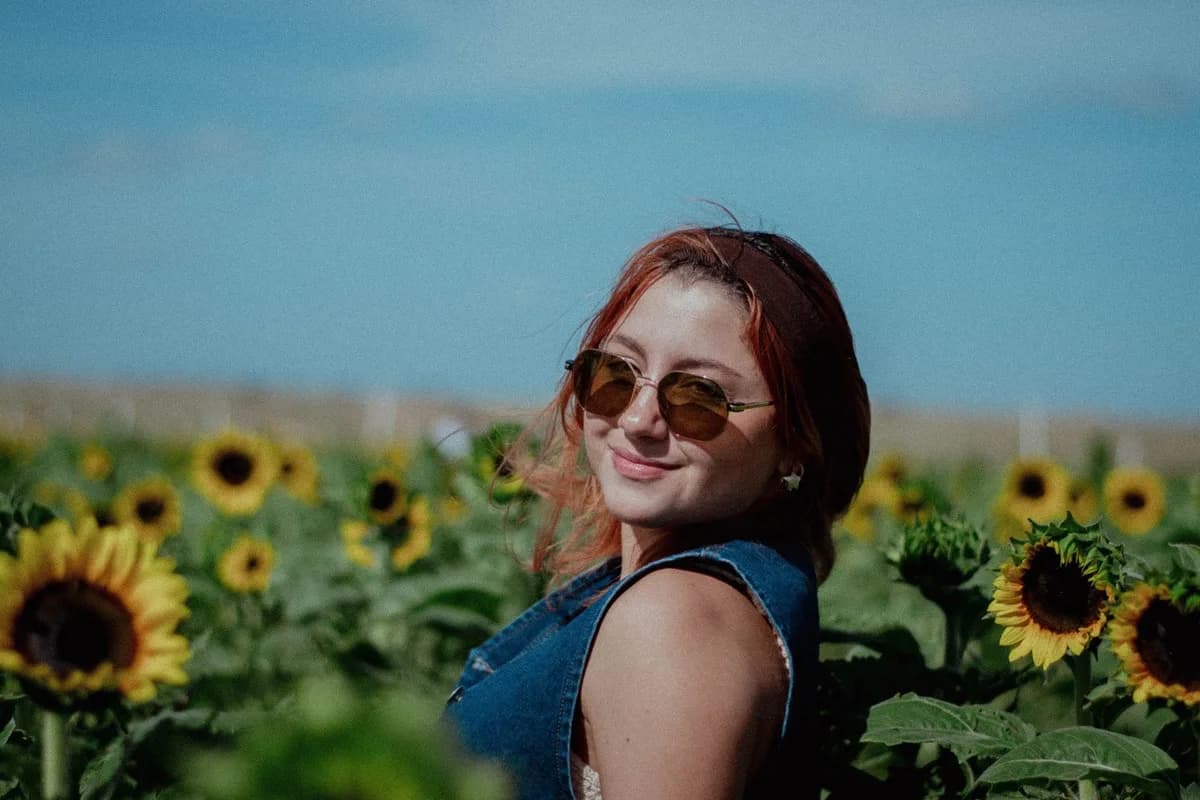 A woman with sunglasses in a vibrant sunflower field under a clear blue sky.