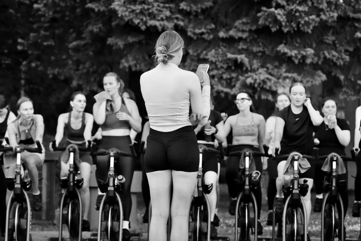 A group of women in an outdoor spinning class with an instructor leading the session.