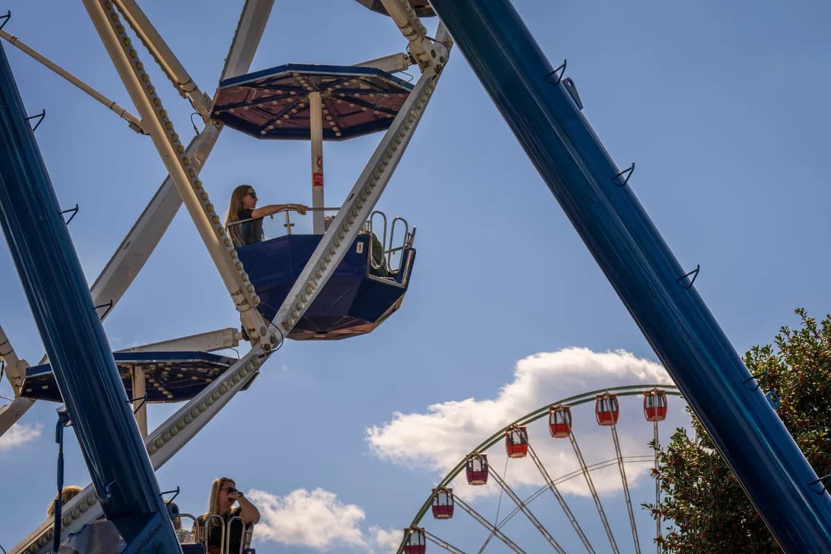 People enjoying a ride on a Ferris wheel under a bright blue sky with clouds.