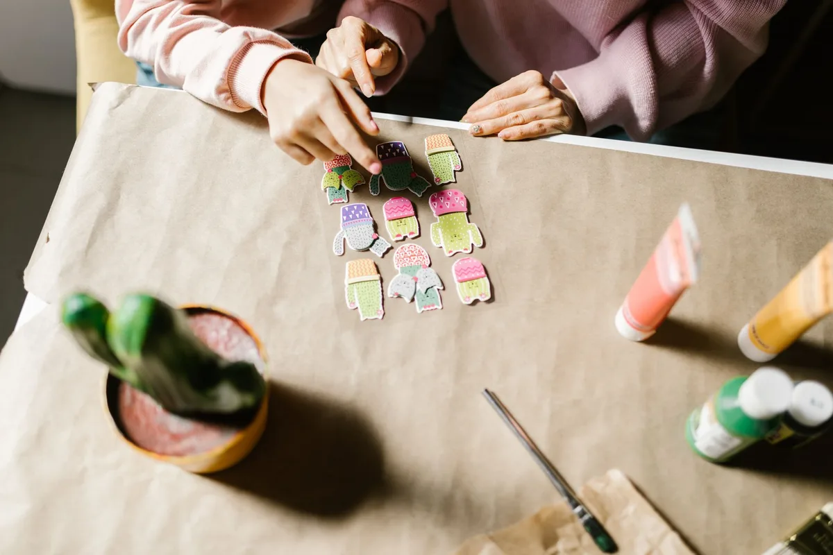 Hands arranging colorful paper cutouts on a table, showcasing creativity and crafting skills.