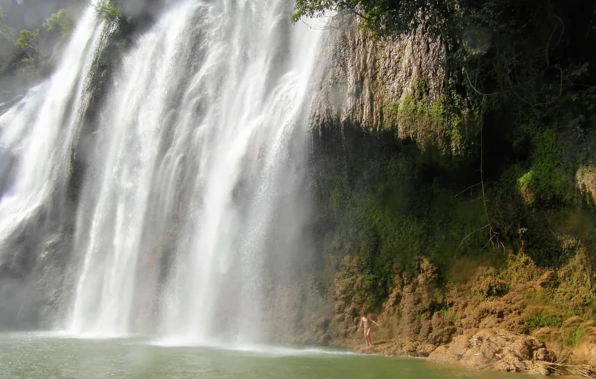 Majestic waterfall cascading over rocky cliffs in Thailand with a serene pool below.