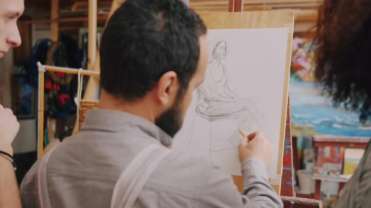 Male artist sketching a figure in an art class, focusing on human form and creativity.