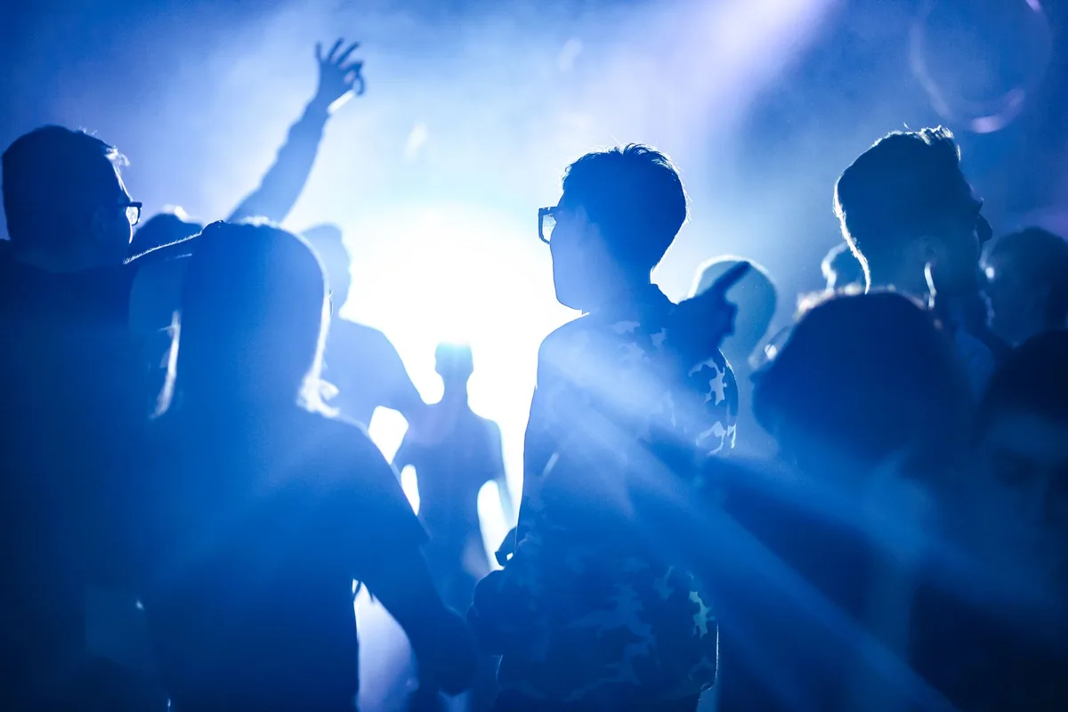 Energetic scene of silhouettes dancing at a nighttime party with bright lights.