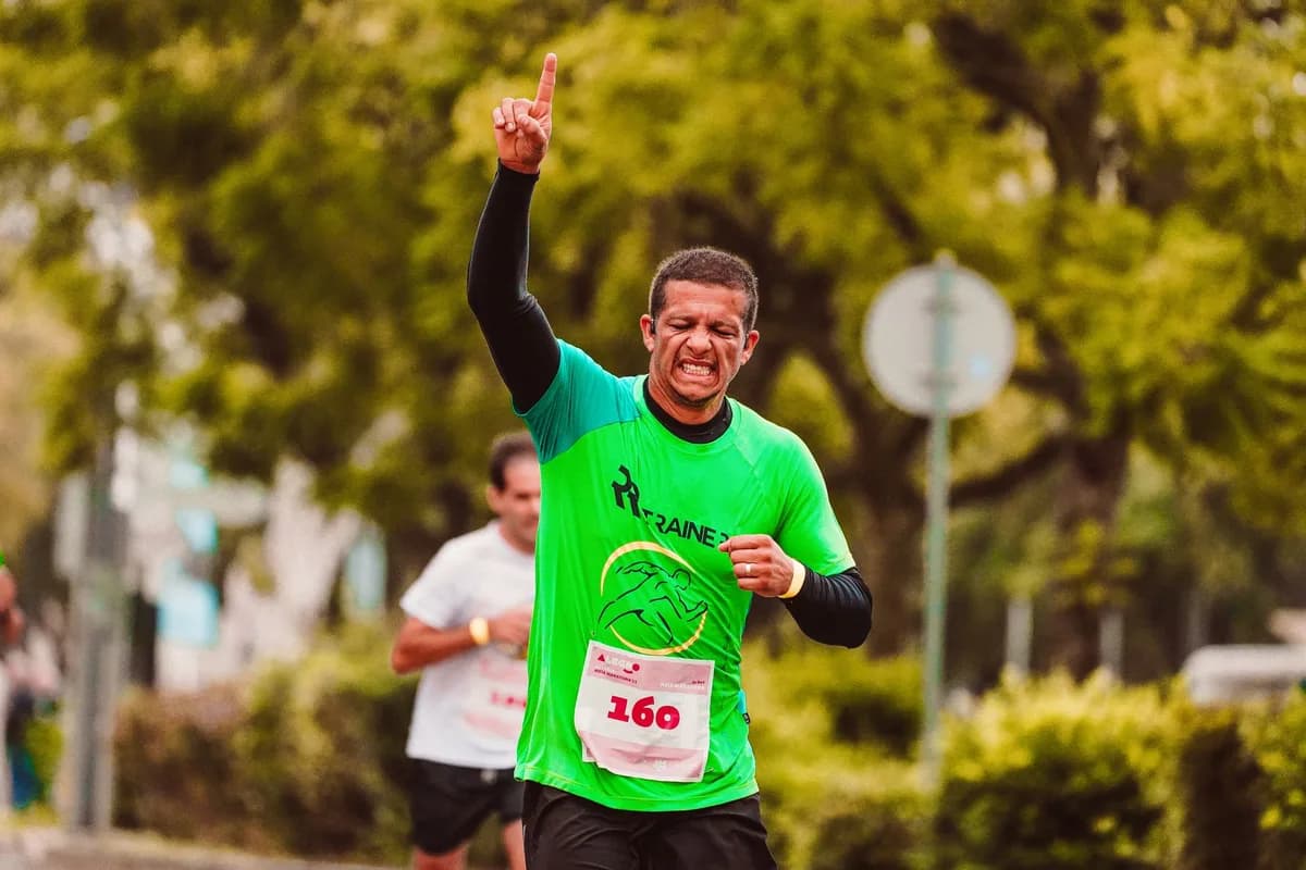 Joyful male runner celebrates a marathon win outdoors, raising arms in triumph.