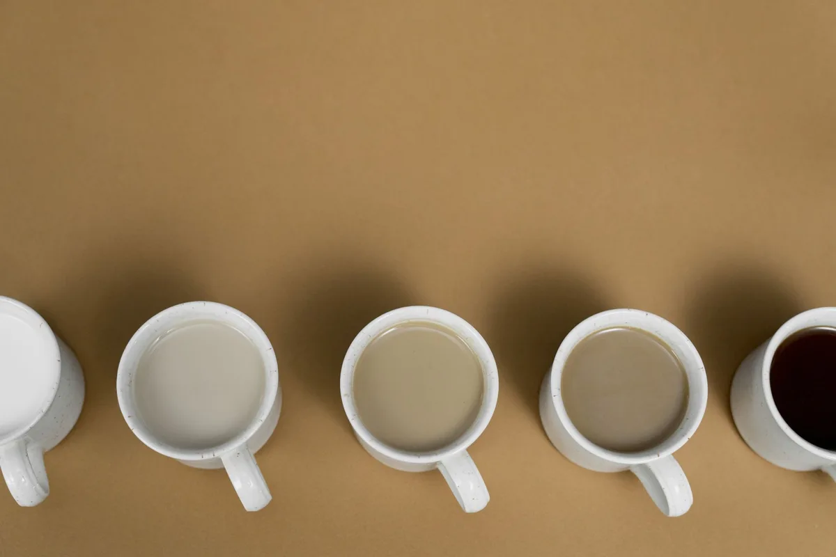 Aesthetic arrangement of coffee mugs with varying milk content on a brown surface, viewed from above.
