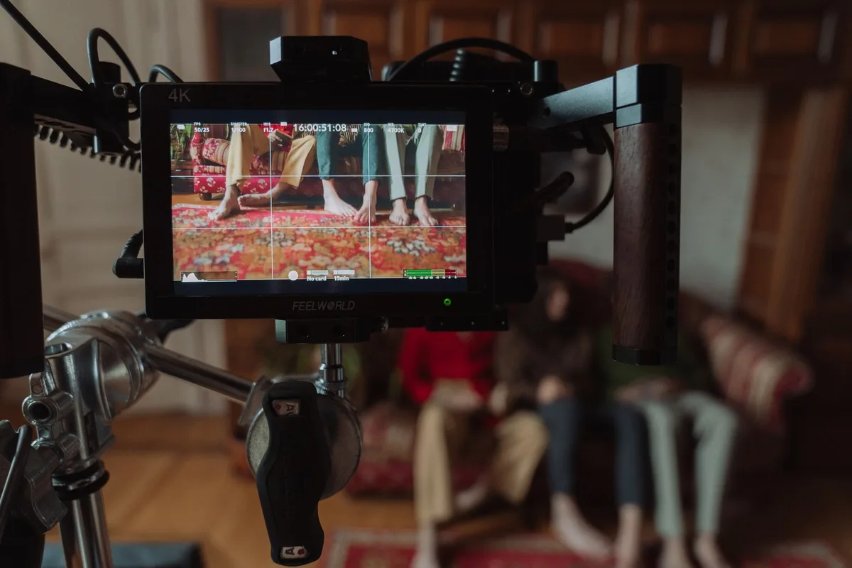 Film set monitor showing a scene with barefoot people sitting on a couch captured during production.
