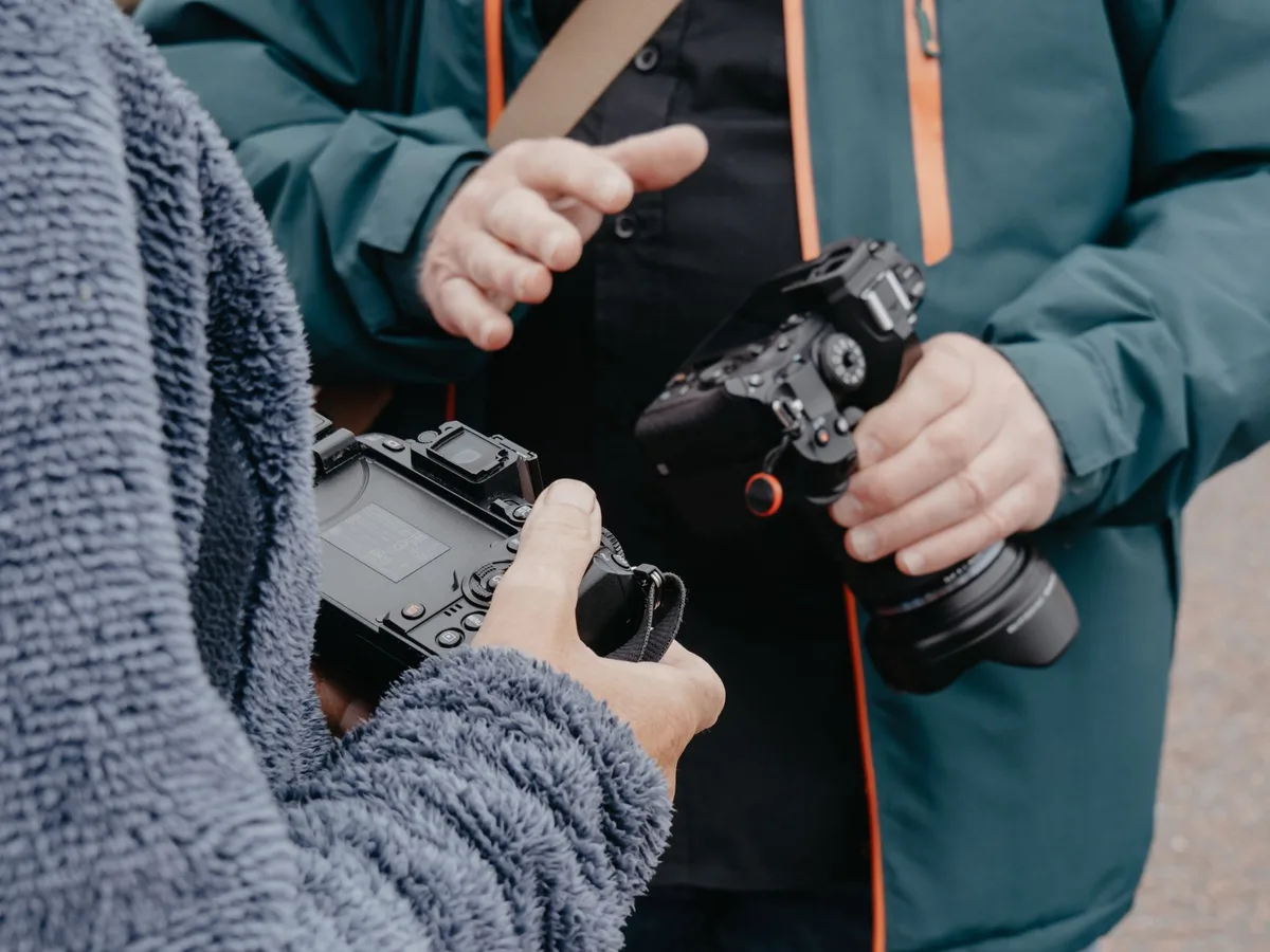 Two people discussing photography while holding cameras outdoors.