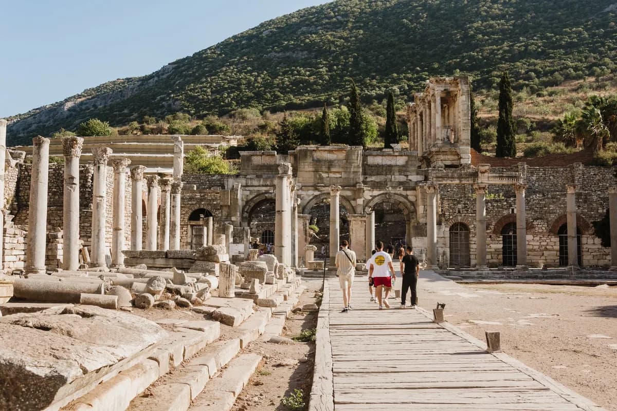Visitors explore the ancient ruins of Ephesus, Turkey with mountain backdrop.