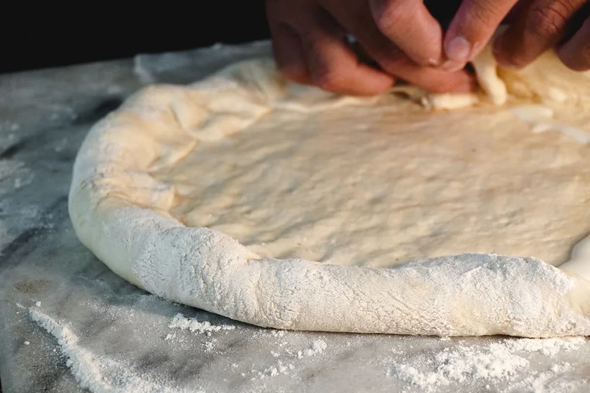 A close-up view of hands preparing pizza dough on a marble surface, showcasing the art of homemade pizza making.