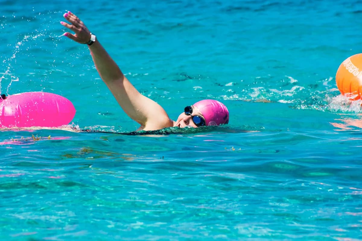 A swimmer with a pink cap and goggles in crystal clear water, perfect for summer sports.