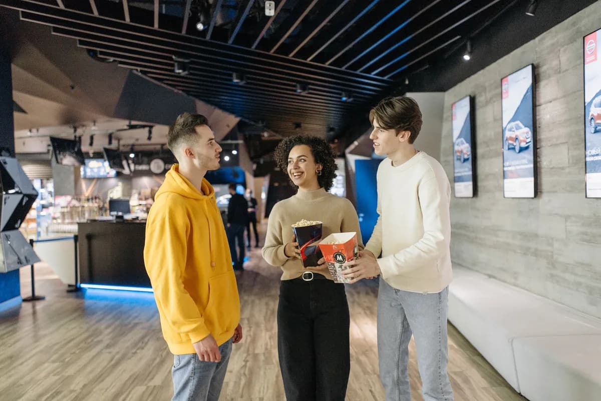 A group of friends enjoying popcorn and conversation in a modern cinema hallway.
