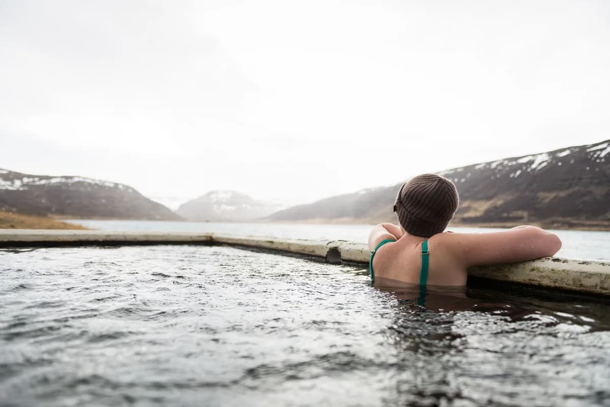 A person relaxes in a hot spring pool surrounded by snowy mountains and serene landscape.