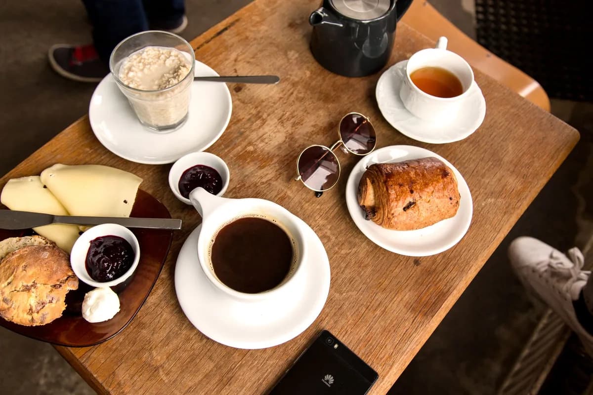 A cozy breakfast setting featuring coffee, pastry, and tea on a wooden table in a cafe.