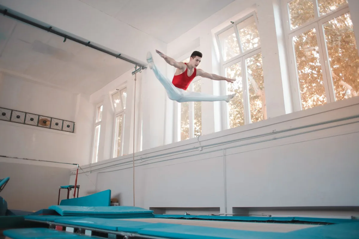 Young sportsman in sportswear doing split in air while jumping on trampoline in gym