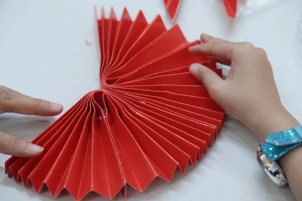 Two hands folding red paper into a decorative pattern, showcasing creativity and skill.