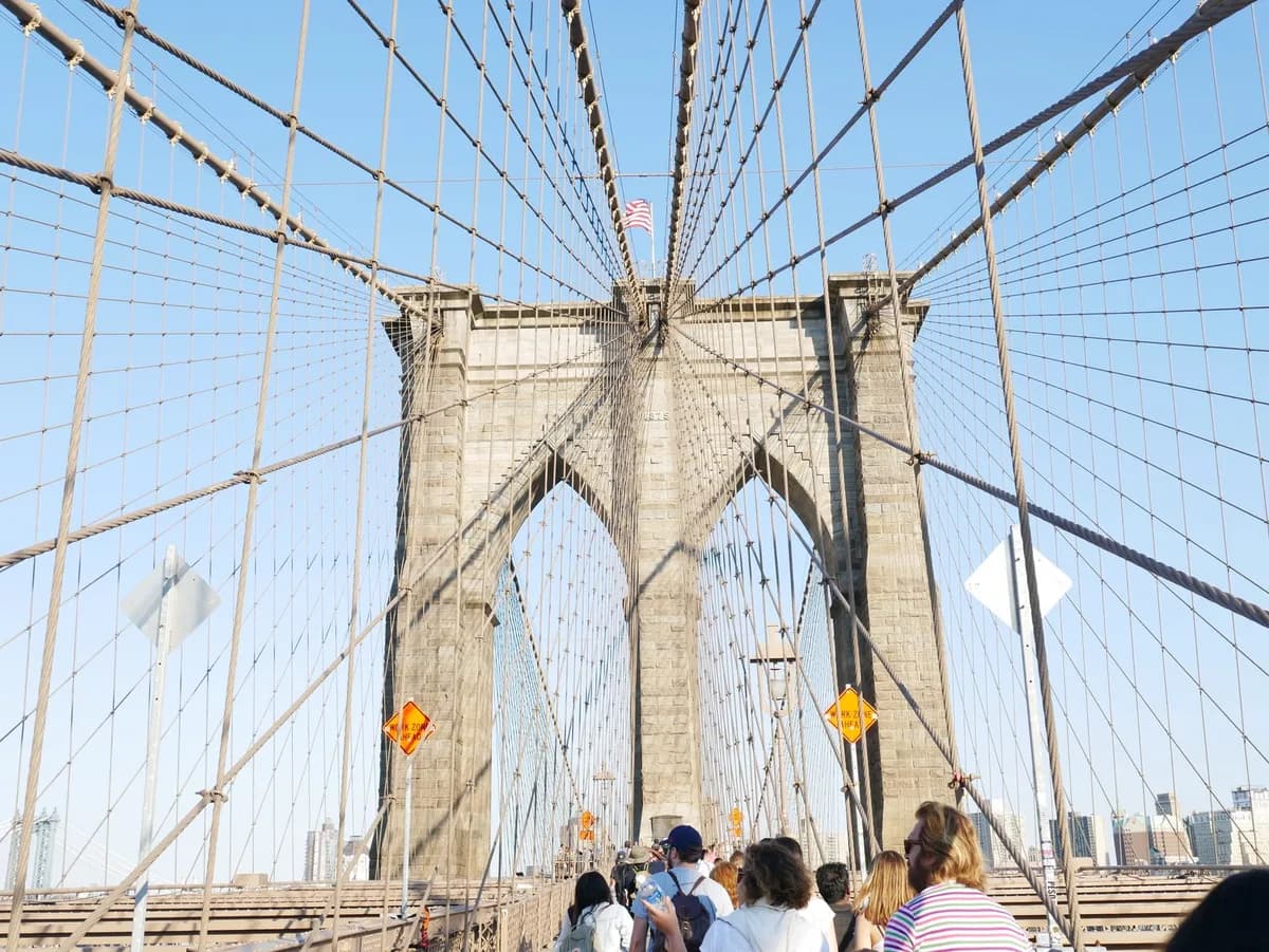 View of pedestrians walking on the Brooklyn Bridge, capturing its iconic architecture against a clear sky.