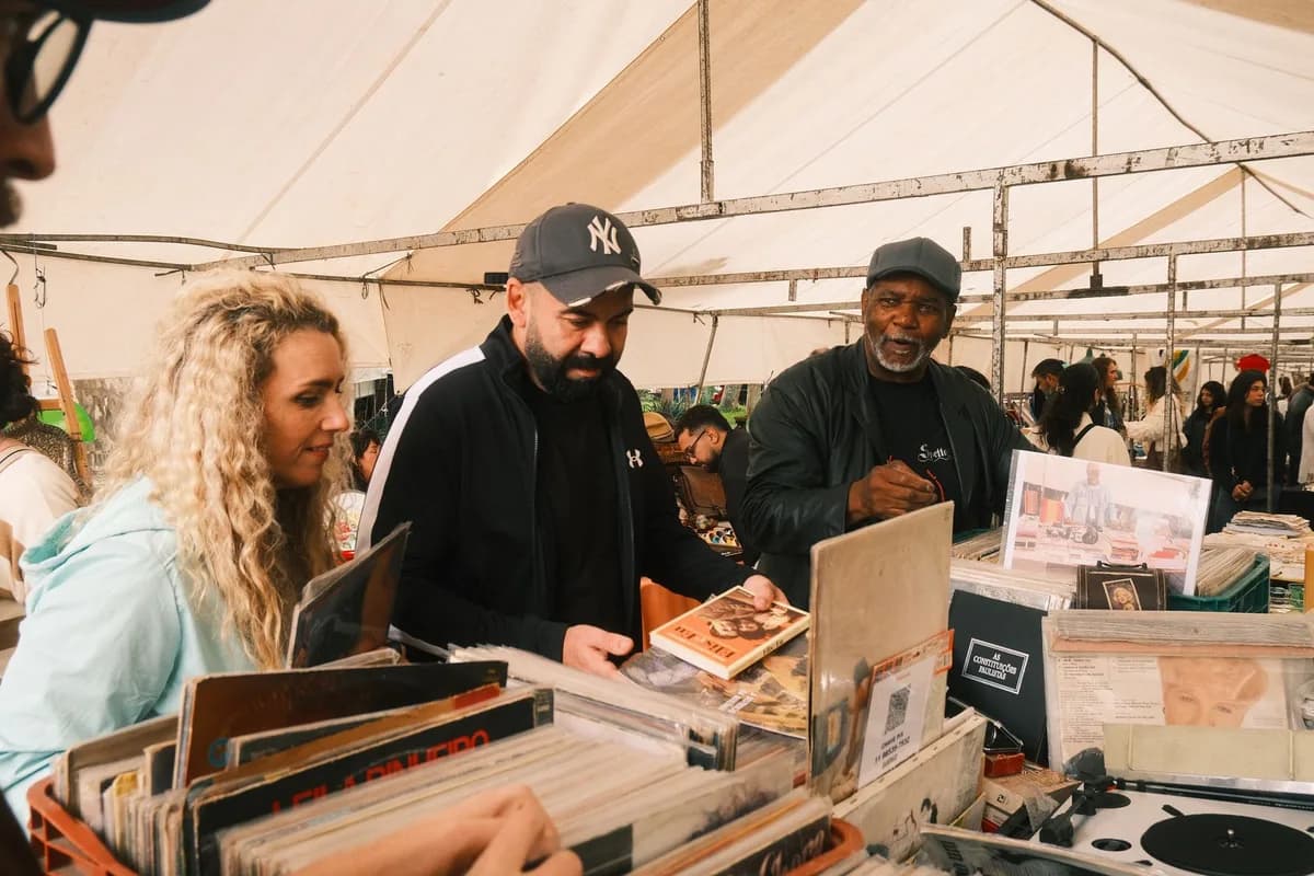 A diverse group browsing records at an outdoor market under a tent.