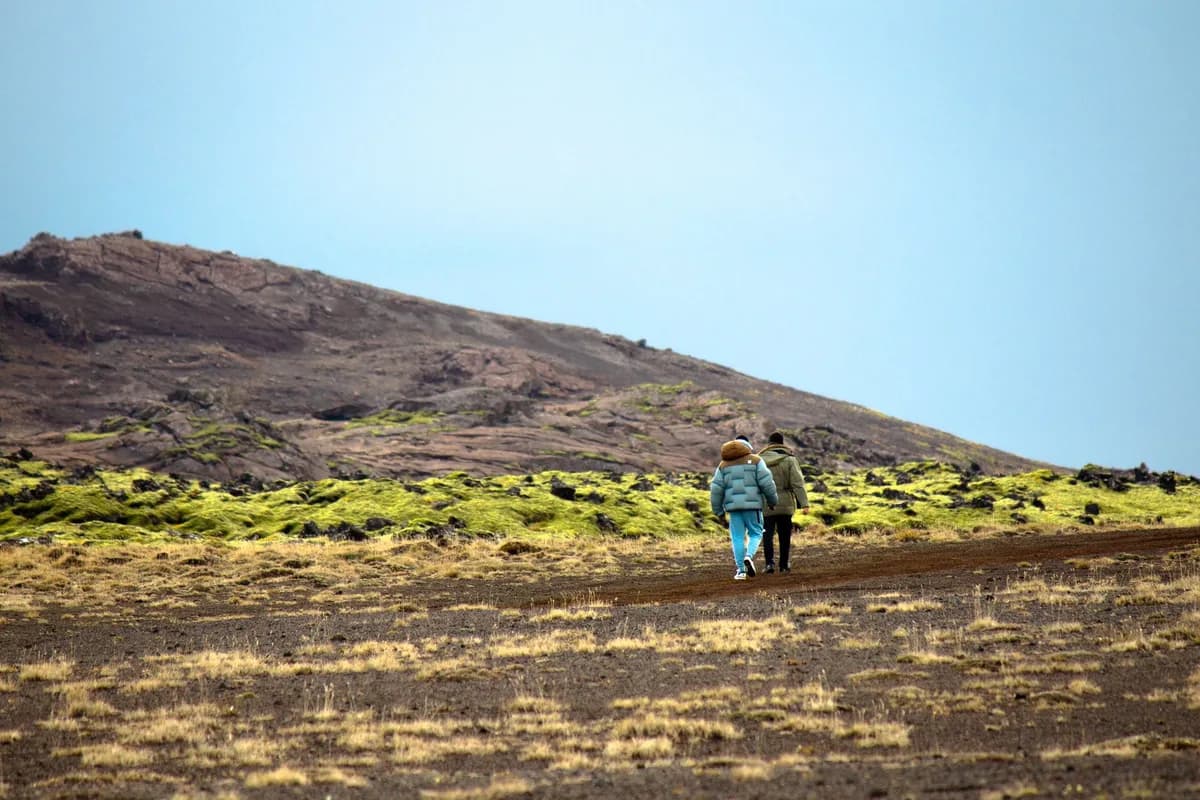 Two people hiking across a rugged volcanic landscape in Iceland.