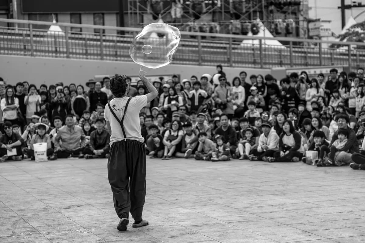A street performer engages a large audience with an impressive giant bubble act.