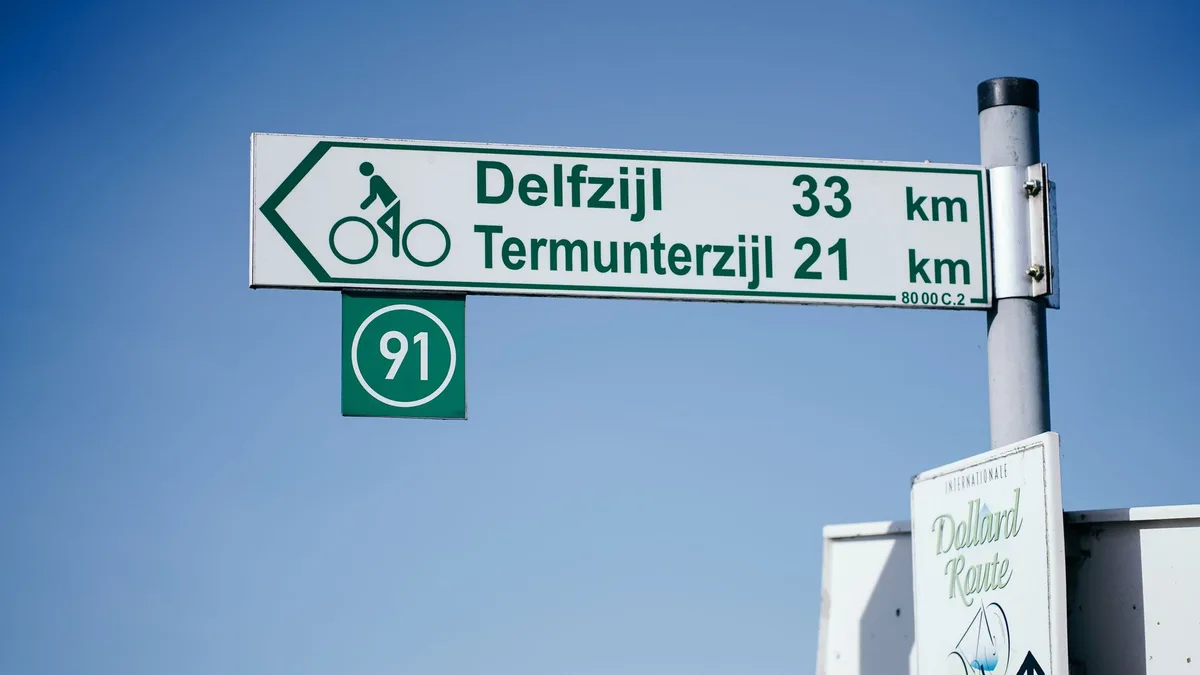 Cycling route sign in Groningen, indicating directions to Delfzijl. Captured on a clear day.
