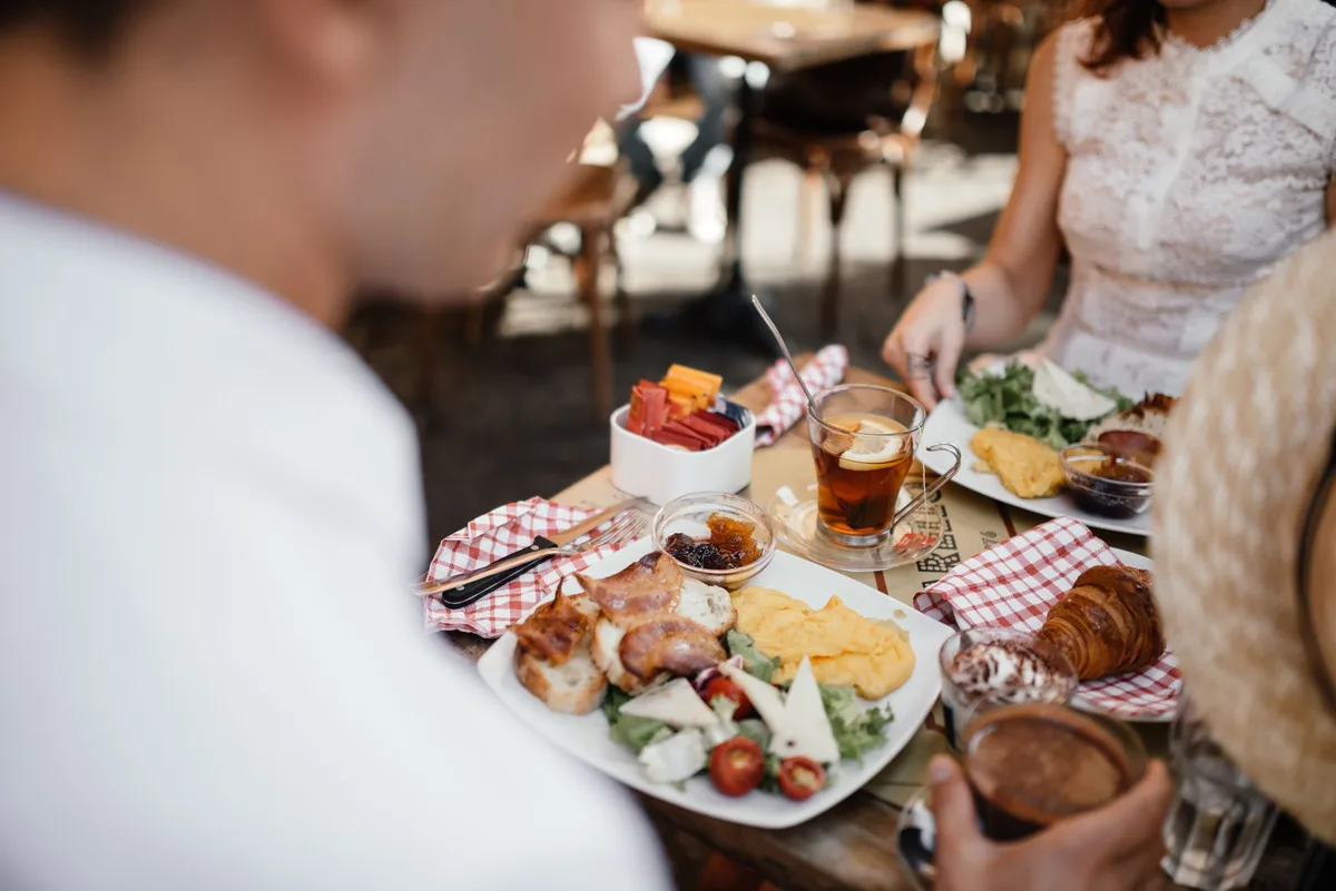Friends enjoying brunch with tea and coffee at an outdoor café, sharing lively conversation and delicious meals.
