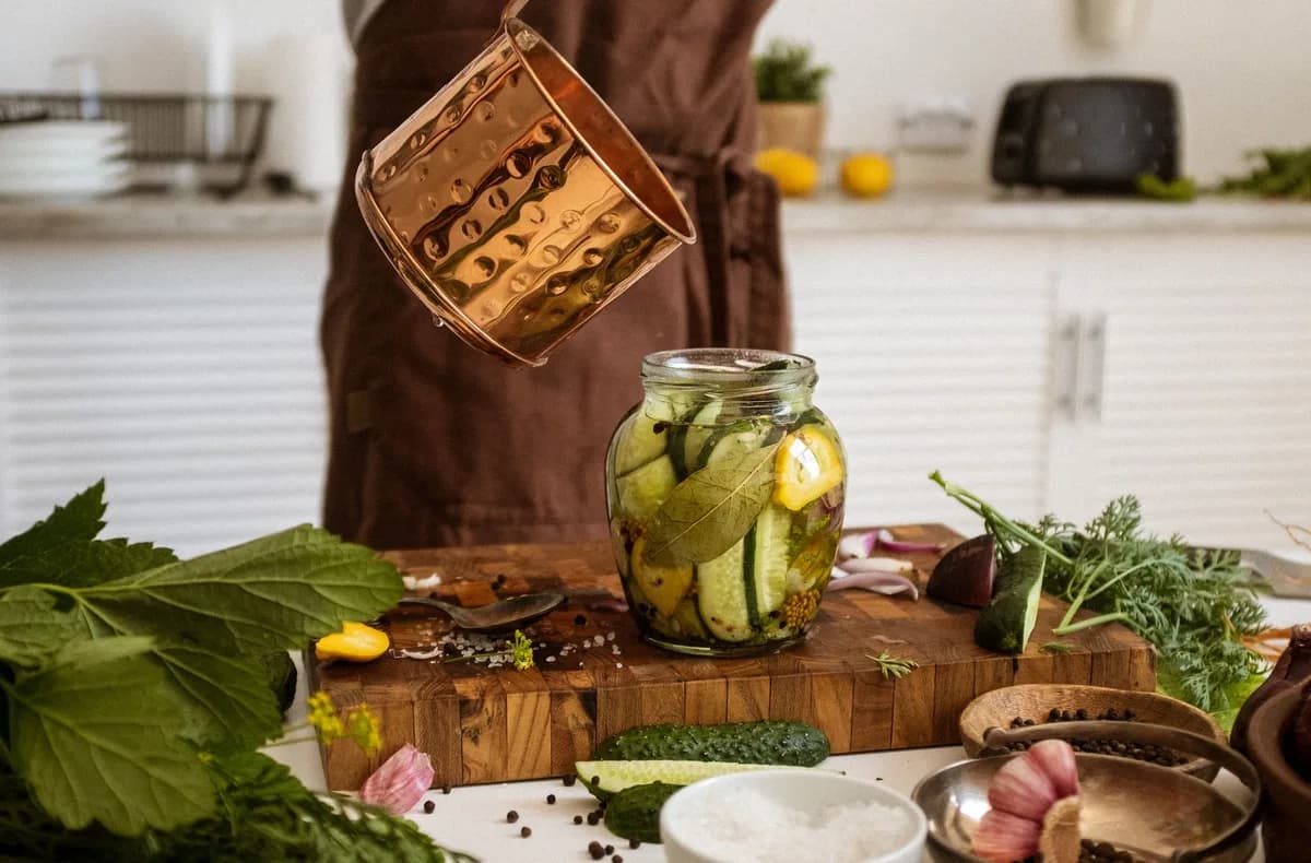A person preparing homemade pickles using fresh cucumbers and herbs in a rustic kitchen setting.