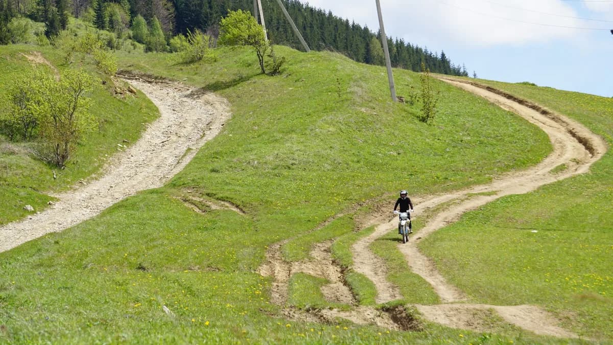 Person riding a motorbike on a scenic mountain trail in a lush forest setting.