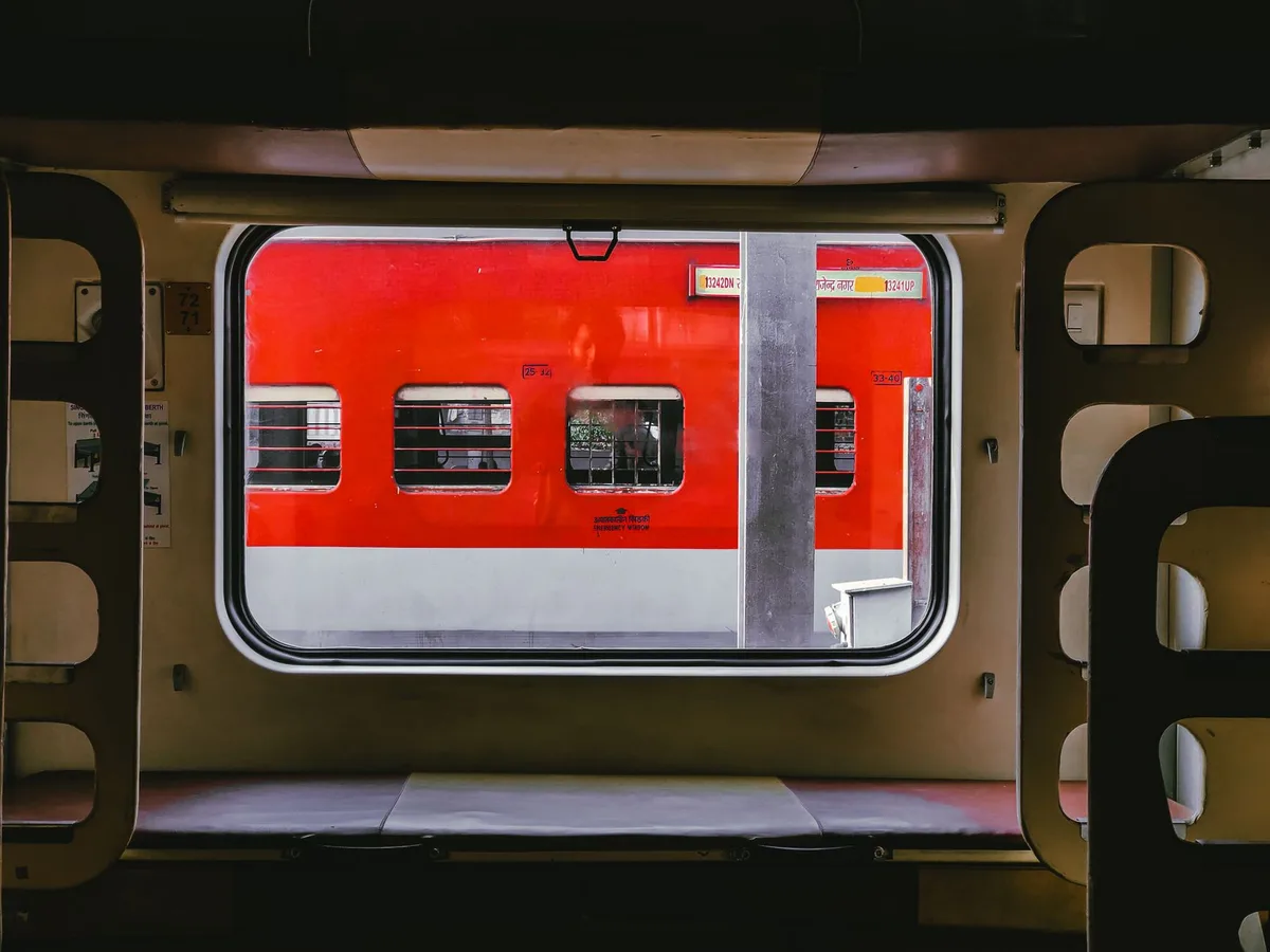 A vibrant red train viewed from another train window at a station, showcasing public transportation.