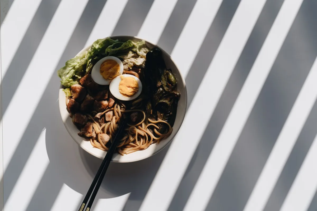 A bowl of ramen with egg, meat, and greens, captured with dramatic lighting and shadows.