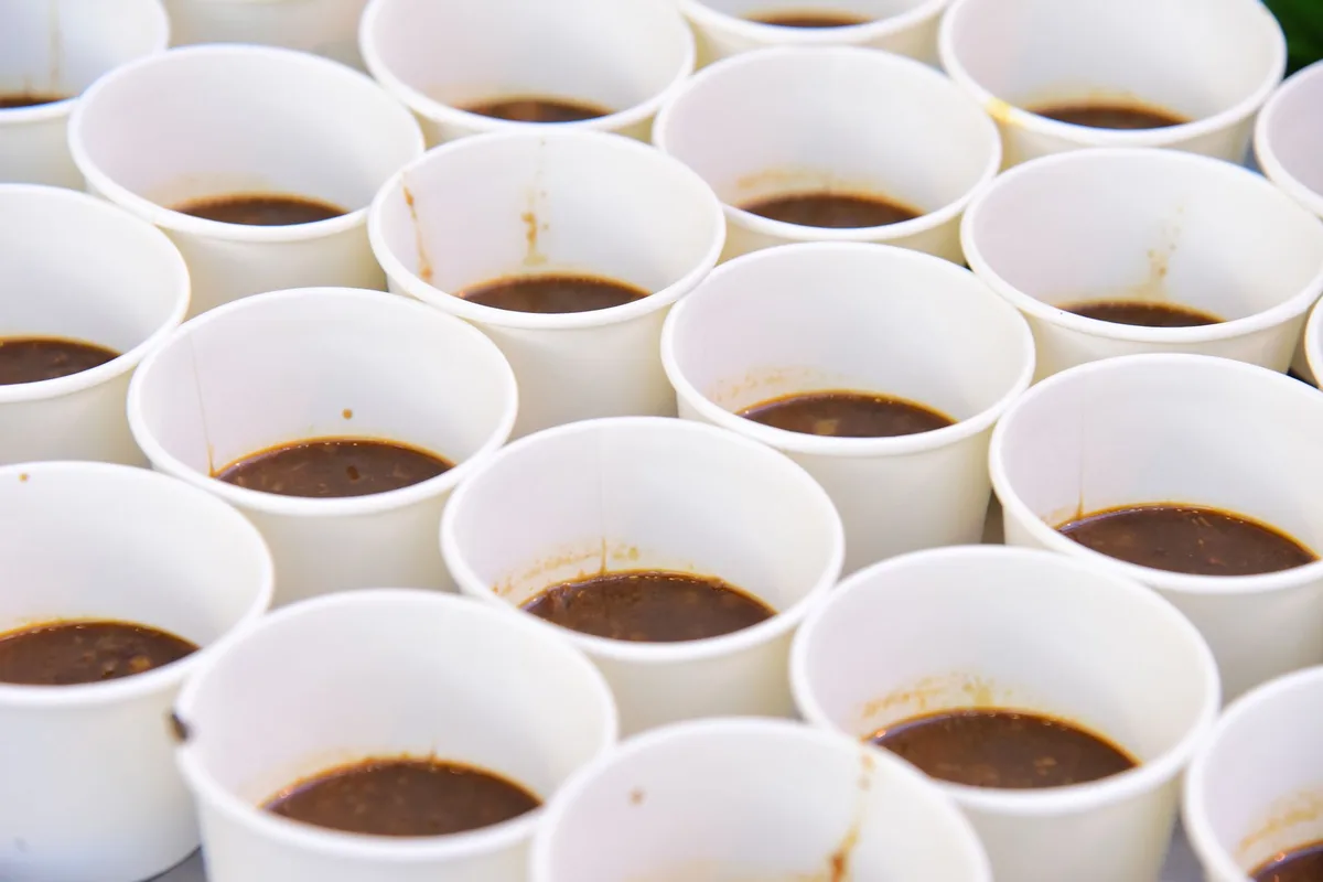 Close-up of multiple white paper cups containing brown liquid, arranged uniformly.