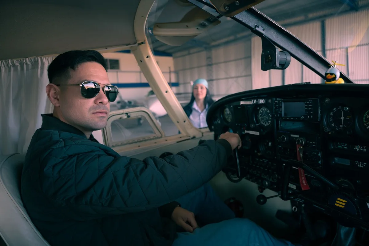 Confident pilot seated in an airplane cockpit, preparing for takeoff inside a hangar.