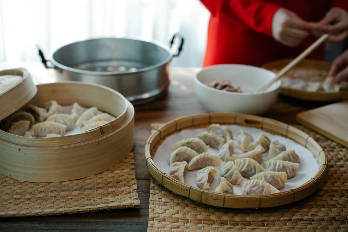 High angle of crop anonymous female folding dumplings while preparing traditional Chinese jiaozi in kitchen at home