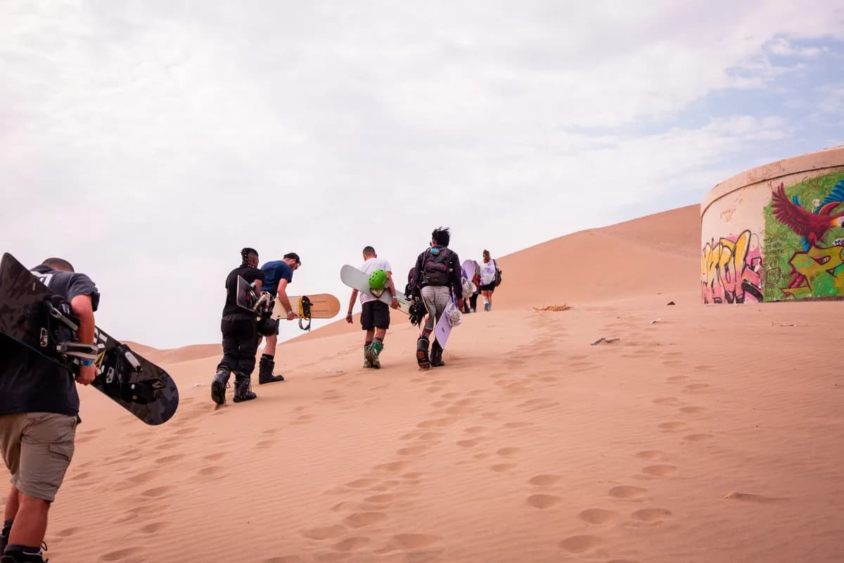 A group enjoying sandboarding in the scenic Ica desert with vibrant graffiti art.