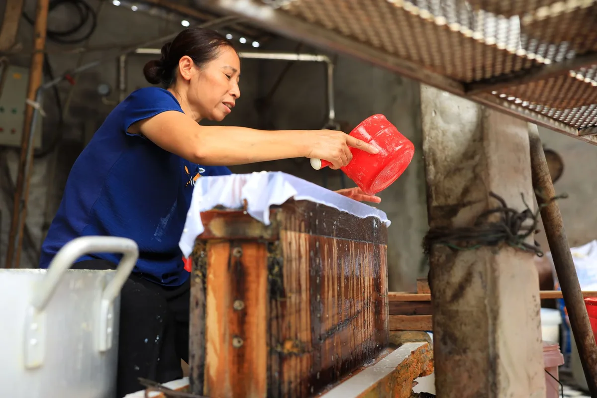 Asian woman skillfully crafting paper in a rural setting, showcasing traditional craftsmanship.