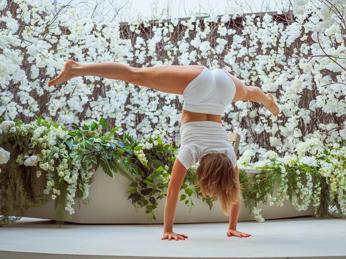 Woman performing a handstand surrounded by vibrant flowers, showcasing fitness and grace.