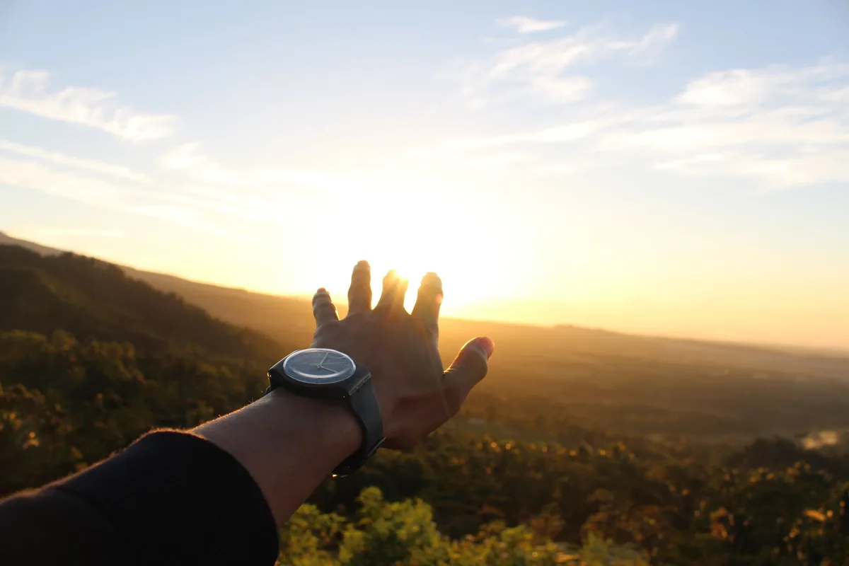 A hand reaching towards a vibrant sunrise over lush landscapes in Central Kalimantan.