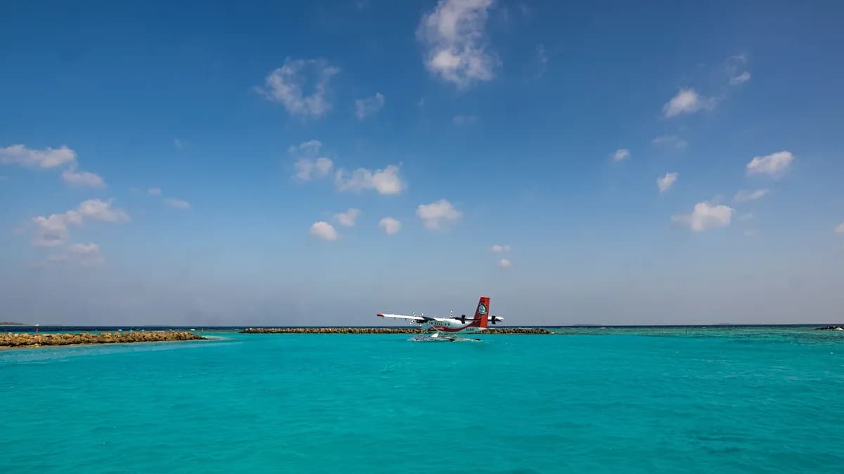 A seaplane glides over vibrant turquoise waters under a bright blue sky in the Maldives.