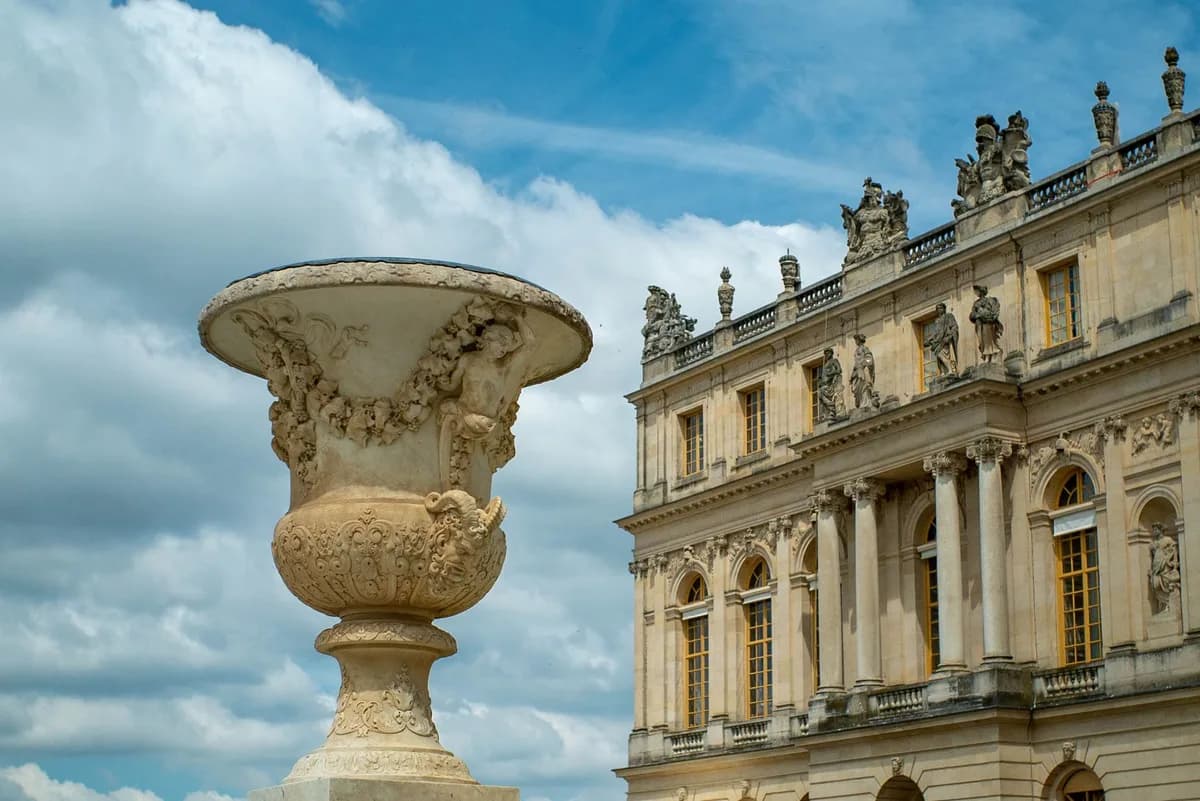 Majestic view of Versailles Palace with an ornate vase, under a blue sky. Perfect for travel and architecture enthusiasts.