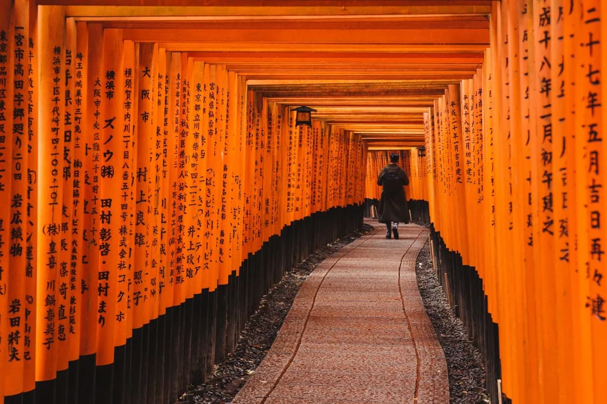 A person walking through the iconic torii gate pathway at Fushimi Inari Taisha in Kyoto, Japan.
