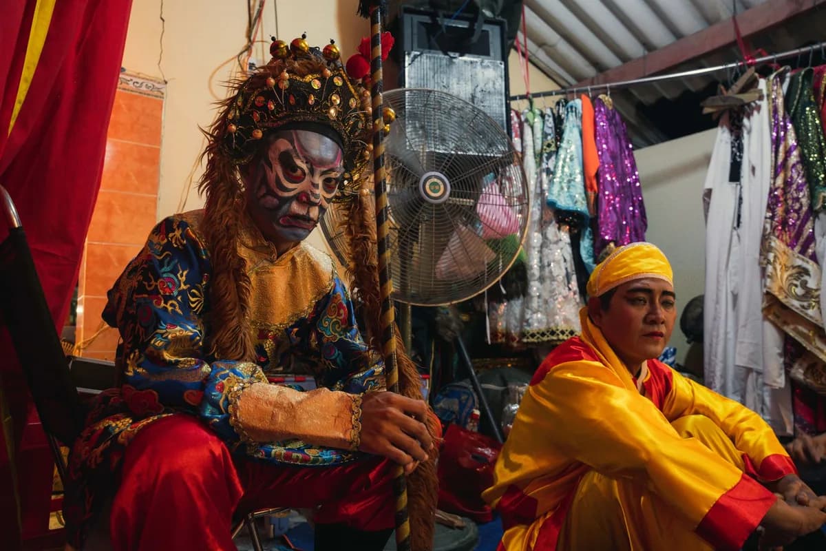 Two Chinese opera performers in ornate costumes preparing backstage before a performance.