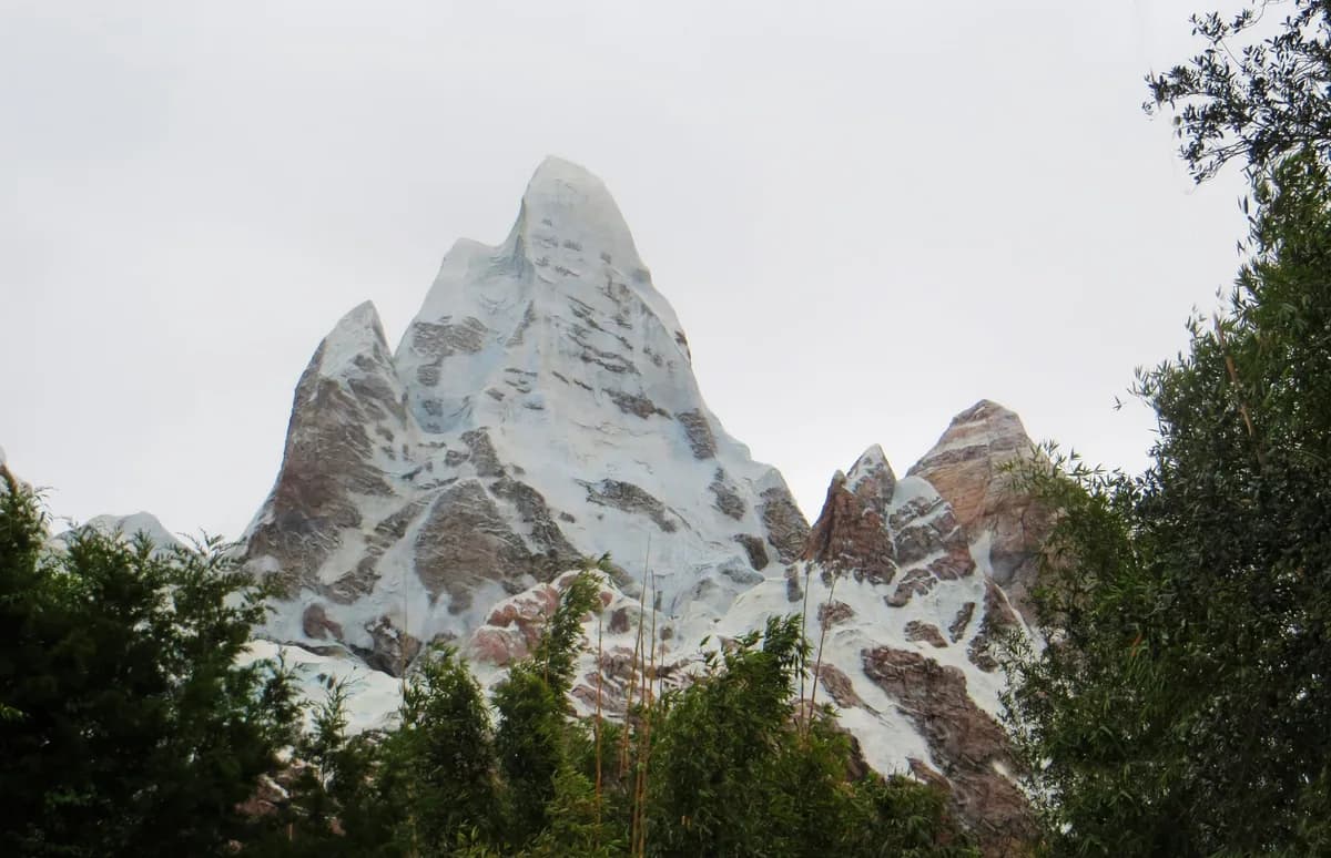 Scenic snow capped mountain peaks surrounded by lush green trees under a clear sky.