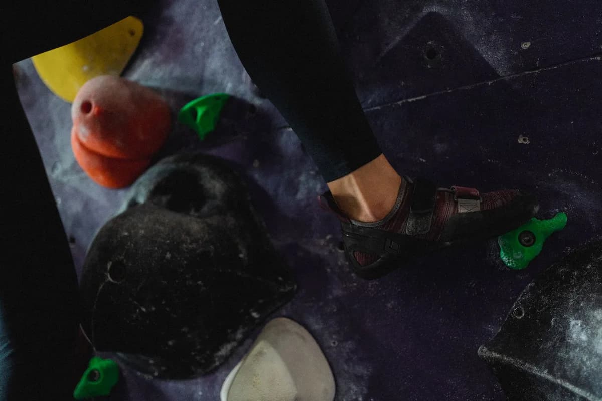 Crop anonymous brave alpinist in sports shoes and leggings climbing on grips in fitness center