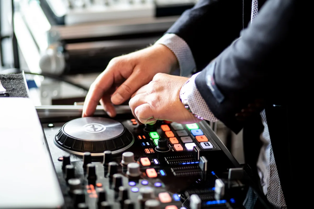 Unrecognizable male musician standing near table with audio console and touching turntable while performing record in modern studio during daytime