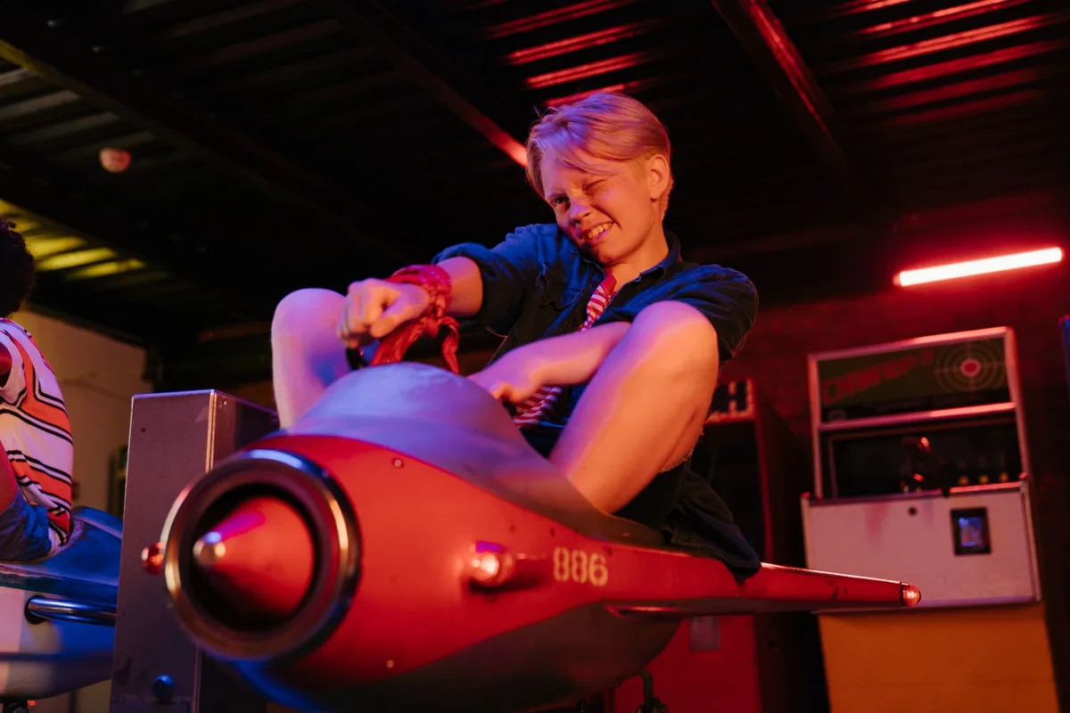 A cheerful young boy enjoying a ride on a toy plane in an indoor amusement park setting.