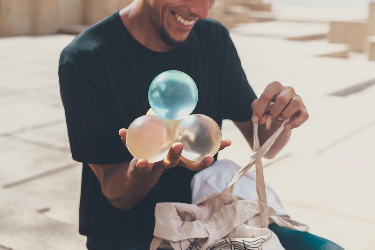A joyful performer juggling transparent spheres outdoors, showcasing a talent for balance.