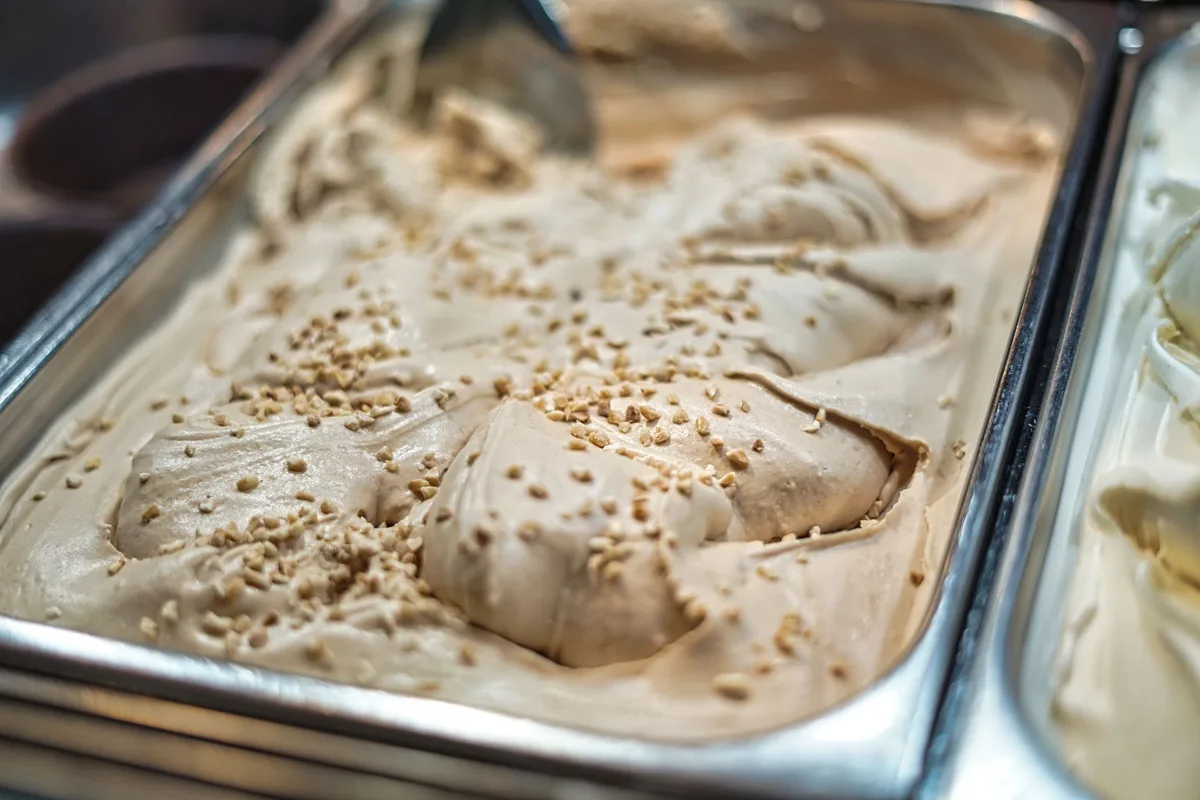 Close-up of creamy hazelnut gelato with sprinkles in a metal container, ready to serve.