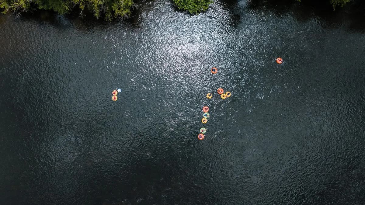 Aerial shot of people relaxing in tubes on a serene river during summer.