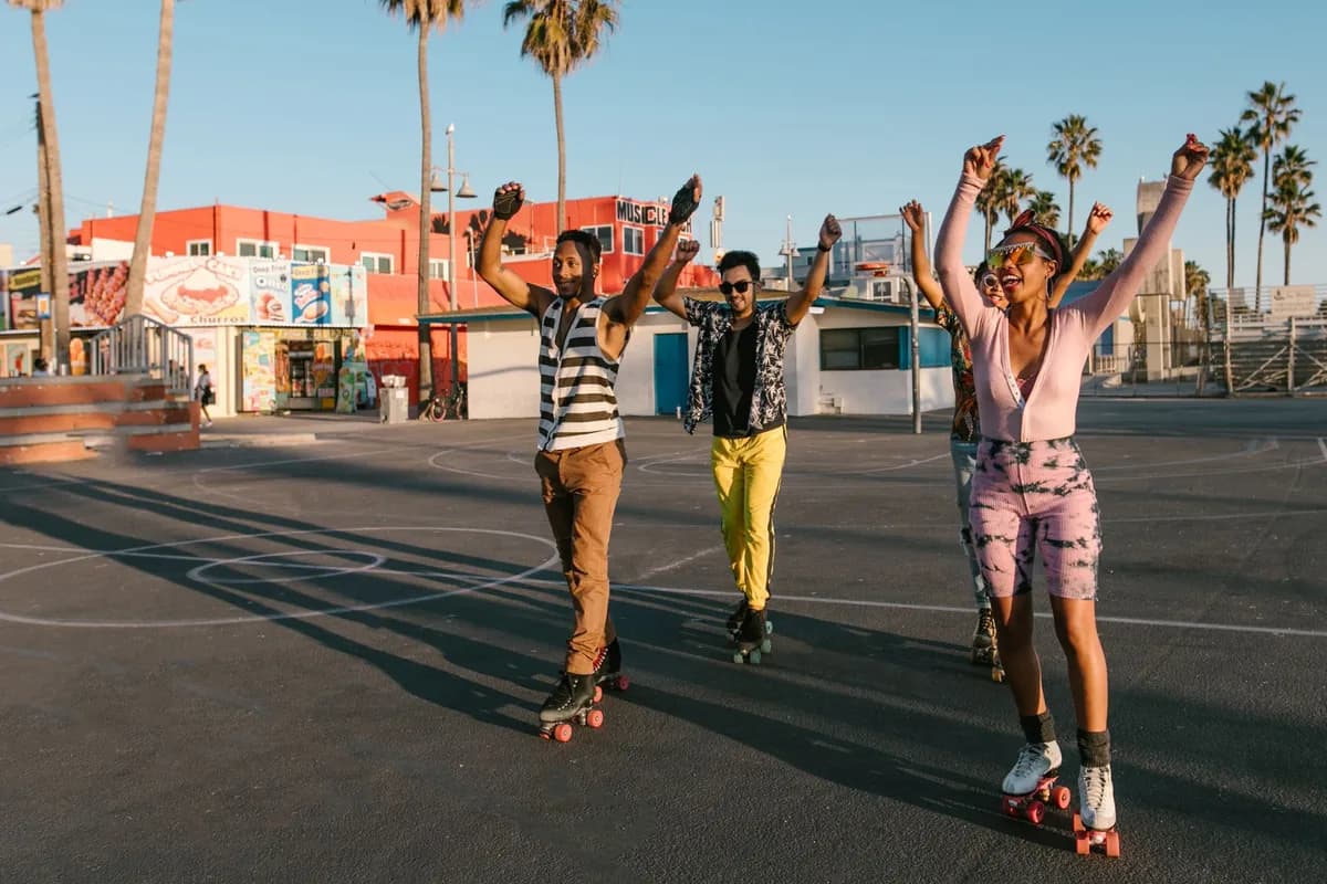Joyful group of friends roller skating outdoors with arms raised, enjoying a sunny day.