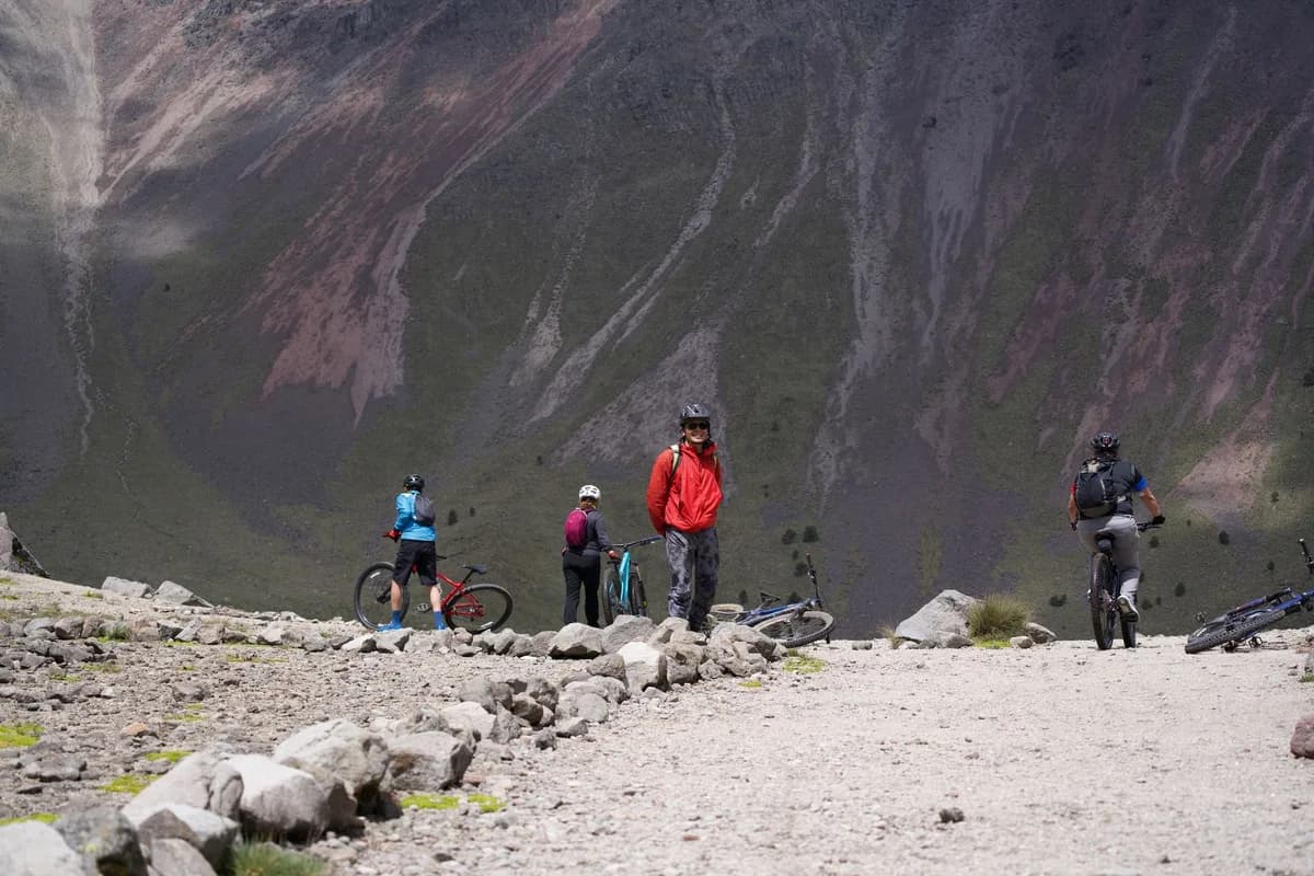 Group of cyclists mountain biking on a rugged hilltop trail amidst dramatic landscapes.